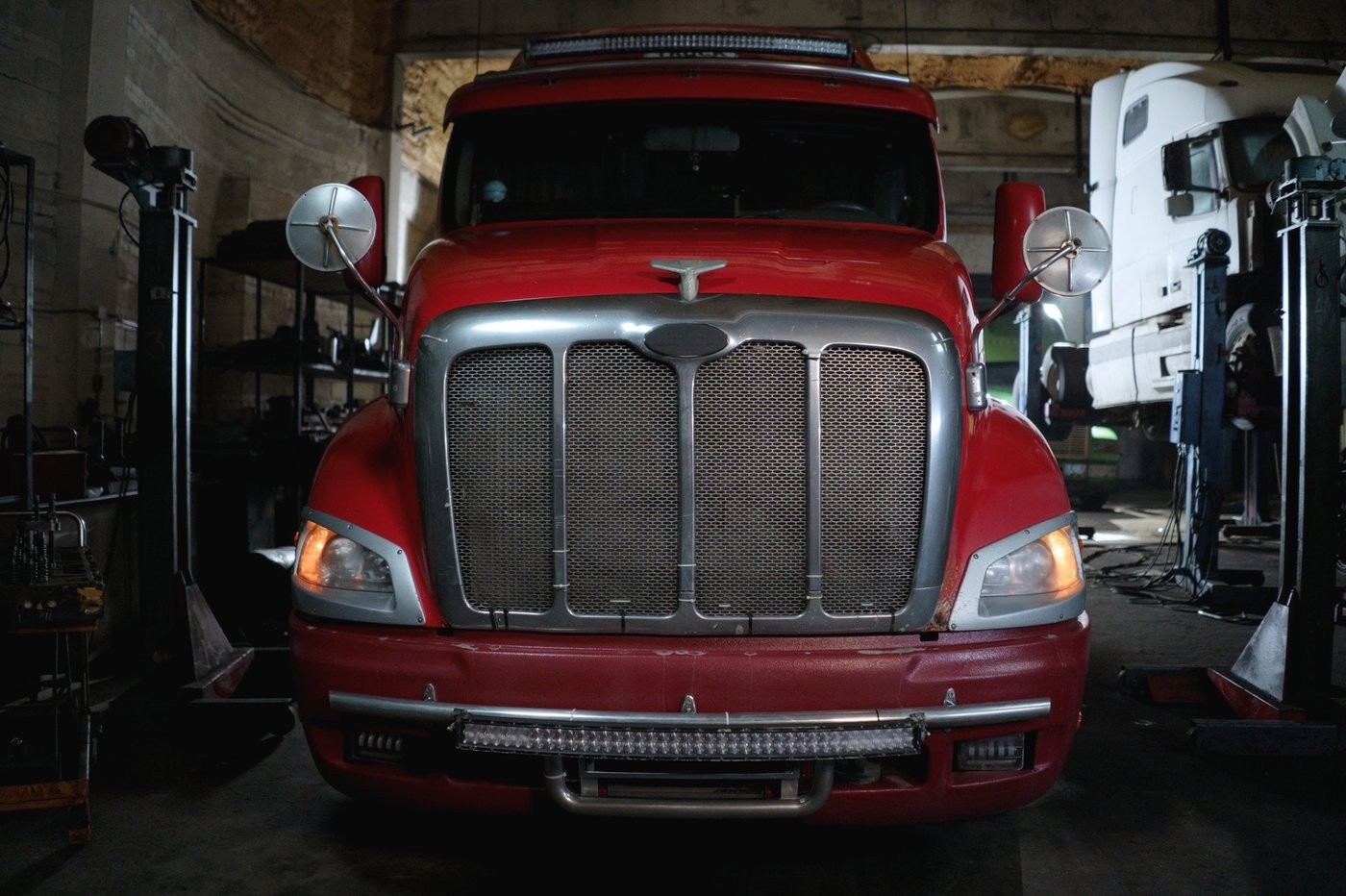 A conventional-cab truck parked nose-on inside a service shop.